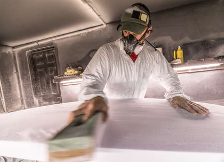 Male carpenter using sandpaper on surfboard in surfboard maker's workshop