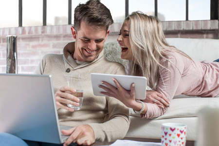 Couple at home, man using laptop, woman holding digital tablet, laughingの写真素材