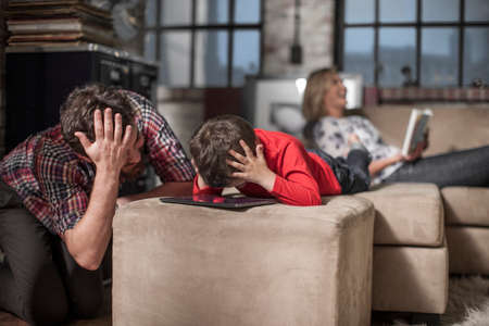 Father and son touching head in disbelief, over digital tabletの写真素材