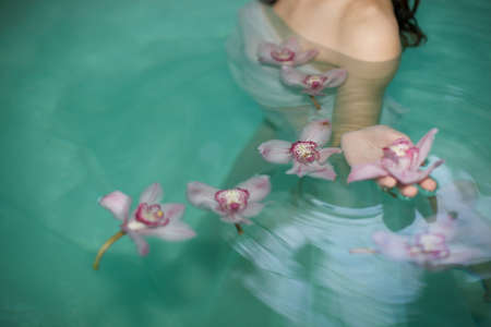Cropped shot of young woman in spa swimming pool with floating purple orchidsの写真素材
