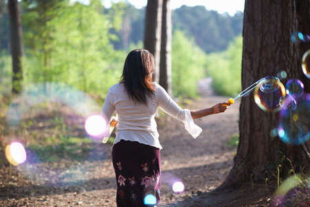 Rear view of woman in forest making bubbles with bubble wand