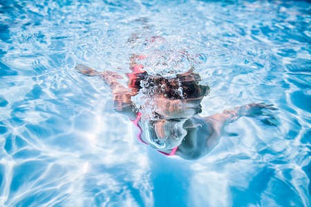 Girl swimming underwater in sunlit swimming poolの写真素材