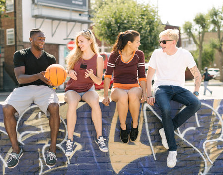 Male and female basketball friends sitting chatting in city skateparkの写真素材