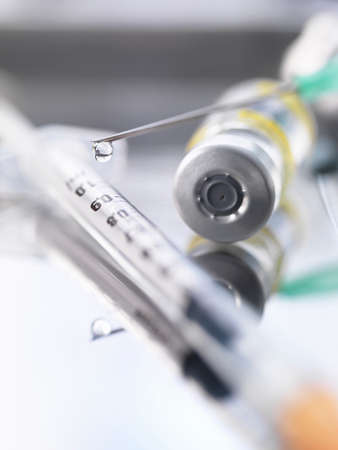 Ampoule containing a drug dose next to a syringe with a droplet of medicine at the end of the needleの写真素材