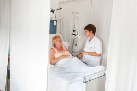 Nurse tending to patient in hospital bedの写真素材