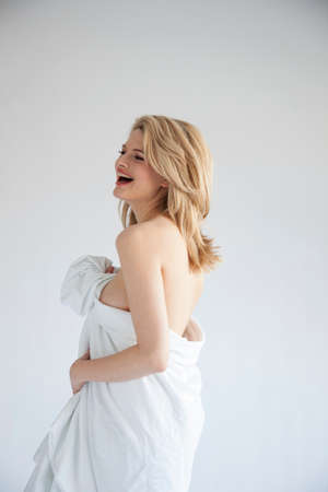 Studio shot of beautiful naked blond young woman wrapped in sheet, laughingの写真素材