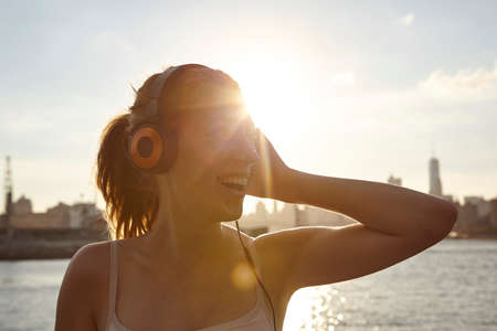 Woman wearing headphones by water smiling, Manhattan, New York, USAの写真素材