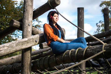 Young woman sitting on wooden climbing frame, wearing headphonesの写真素材