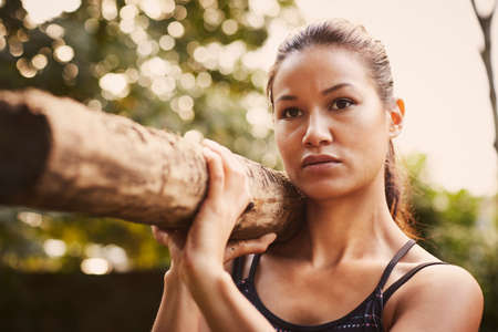 Portrait of woman training,  lifting tree trunk on shoulder in park