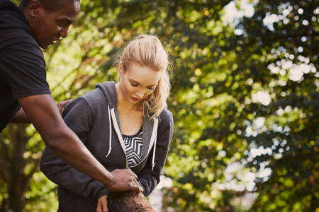 Young woman with personal trainer explaining tree trunk lift in parkの写真素材