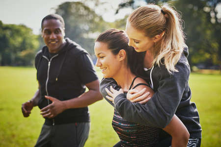 Personal trainer encouraging two women piggy backing in parkの写真素材
