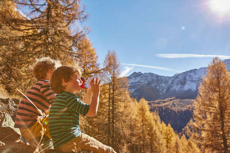 Two boys sitting on rocks, drinking from water bottles, Schnalstal, South Tyrol, Italy