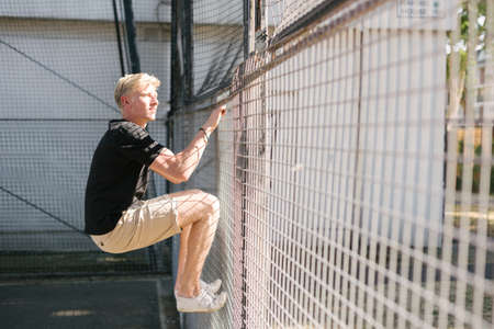 Young man climbing wire fence