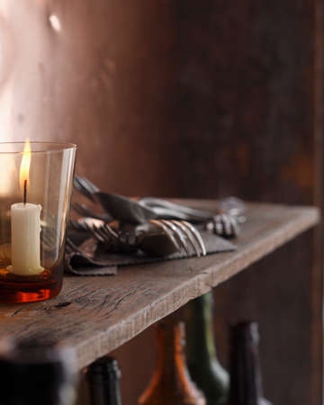 Lit candle and cutlery on shelfの写真素材