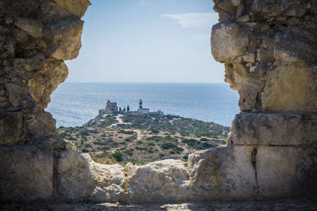 View of lighthouse through hole in stone wall, Cagliari, Masua, Sardinia, Italyの写真素材