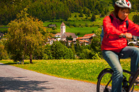 Senior woman cycling along village path in Vinschgau Valley, South Tyrol, Italyの写真素材