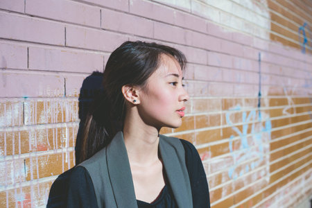 Portrait of young woman leaning against graffiti brick wallの写真素材
