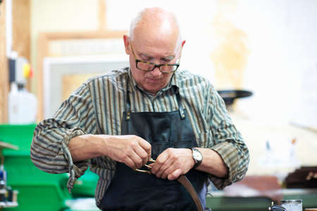 Male worker in leather workshop, polishing belt buckleの写真素材