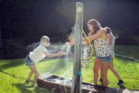 Three adult female friends play fighting sprinkling water hose in gardenの写真素材