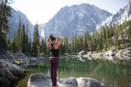 Young woman standing on rock beside lake, looking at view, The Enchantments, Alpine Lakes...