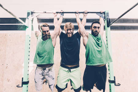Three male cross trainers training on exercise bar in gymの写真素材