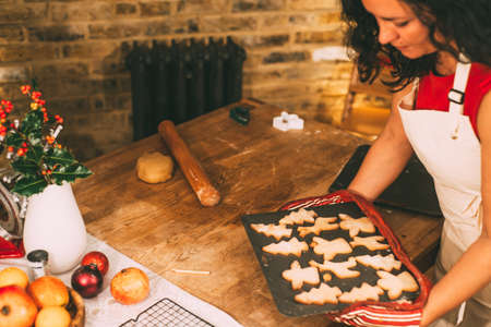 Mature woman carrying fresh Christmas cookies to kitchen counter