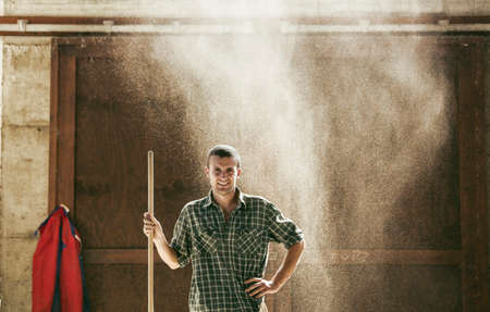 Portrait of young male farmworker in dusty farm barn