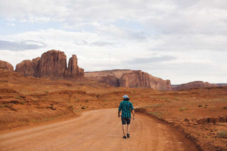 Rear view of young man walking along dirt track, Monument Valley, Arizona, USAの写真素材
