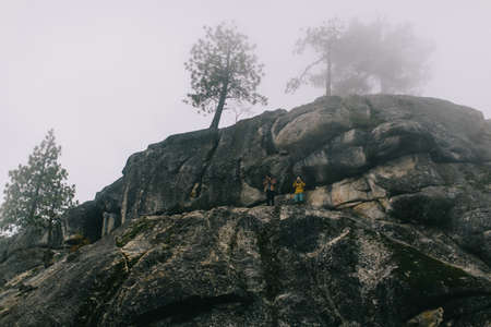 Two young men standing on mountainside, photographing view, near Shaver Lake, California, USAの写真素材