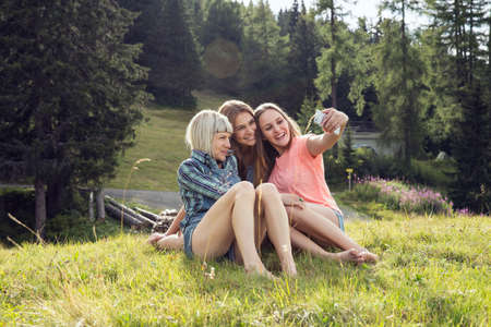 Three female adult friends sitting for smartphone selfie in field, Sattelbergalm, Tirol, Austriaの写真素材