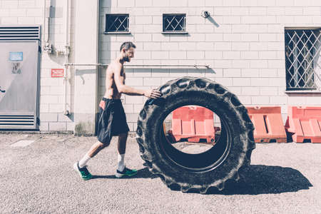 Young male cross trainer pushing large tyre outside gymの写真素材