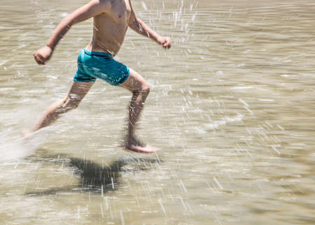 Low section of boy running through shallow waterの写真素材