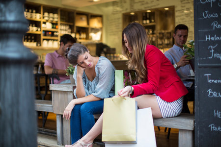 Two young female friends with shopping bags chatting outside cafeの写真素材