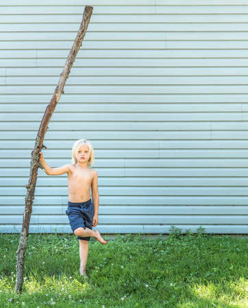 Boy standing on one leg holding stickの写真素材