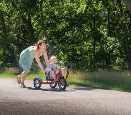 Mother pushing daughter riding tricycleの写真素材