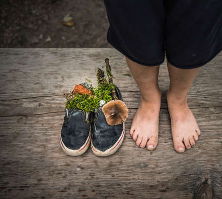 Bare feet of boy next to shoes filled with nature