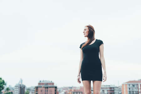 Young woman in mini dress looking over her shoulder above city
