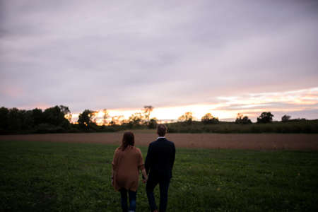 Rear view of romantic couple in field watching sunsetの写真素材
