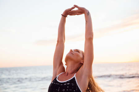 Woman on beach arms raised doing stretching exercise