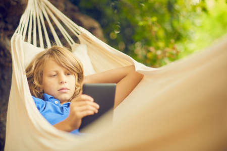Boy reclining in garden hammock browsing digital tabletの写真素材