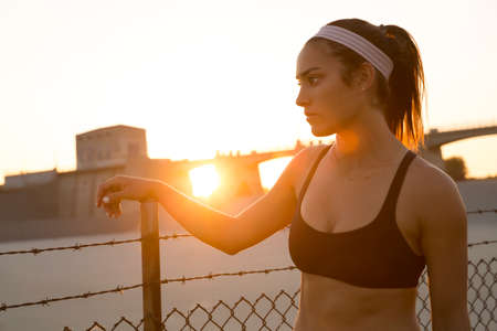 Female athlete daydreaming by wire fence at sunset, Van Nuys, California, USAの写真素材