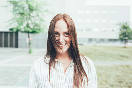Portrait of young woman with freckles and long red hair outside office building