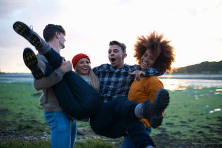 Young man and woman carrying friends at seaside sunsetの写真素材