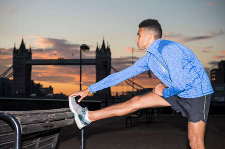 Man stretching by riverside, Tower Bridge in background, Wapping, London, UKの写真素材