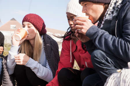 Young adult friends crouching on beach drinking takeaway coffee, Western Cape, South Africa