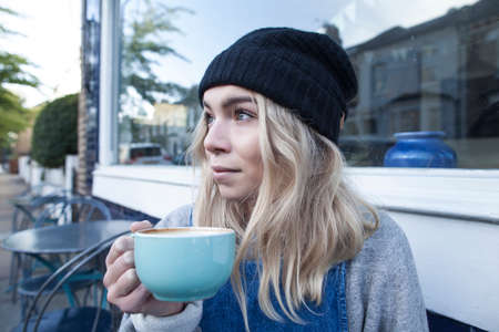 Young woman sitting outside cafe, drinking cup of teaの写真素材