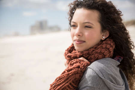 Young woman wrapped in scarf looking out to sea from beach, Western Cape, South Africa