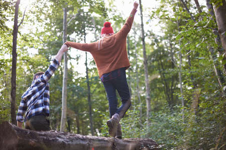 Couple in forest holding hands balancing on fallen treeの写真素材