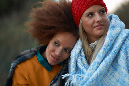 Portrait of two young women huddled in blanket on beach at duskの写真素材