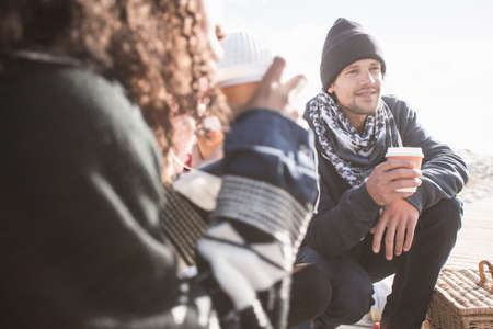 Young adult friends crouching on beach with takeaway coffee, Western Cape, South Africaの写真素材